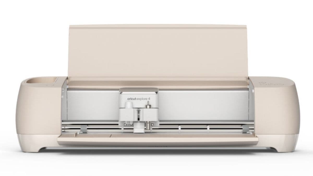 A beige Cricut Explore 4 cutting machine shown from the front with its lid open, revealing the blade housing and tool clamps.