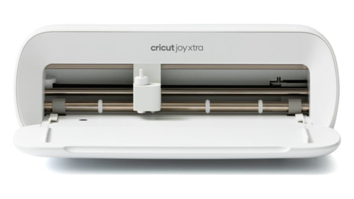A white Cricut Joy Xtra cutting machine shown from the front with its blade housing and open tray visible.