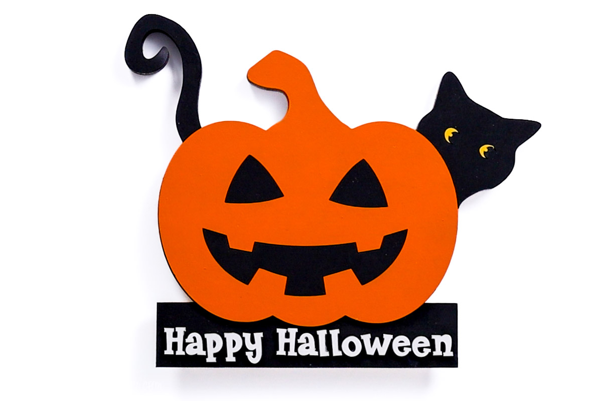 Painted Halloween wood decor featuring a smiling orange jack-o’-lantern with a black cat peeking out, set above a base that reads Happy Halloween.