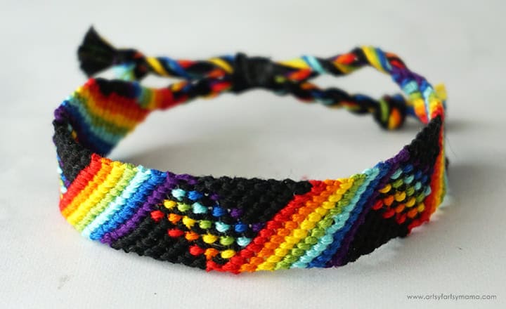 Handmade friendship bracelet with a rainbow chevron pattern woven with black thread, featuring vibrant colors and braided ties at the ends.