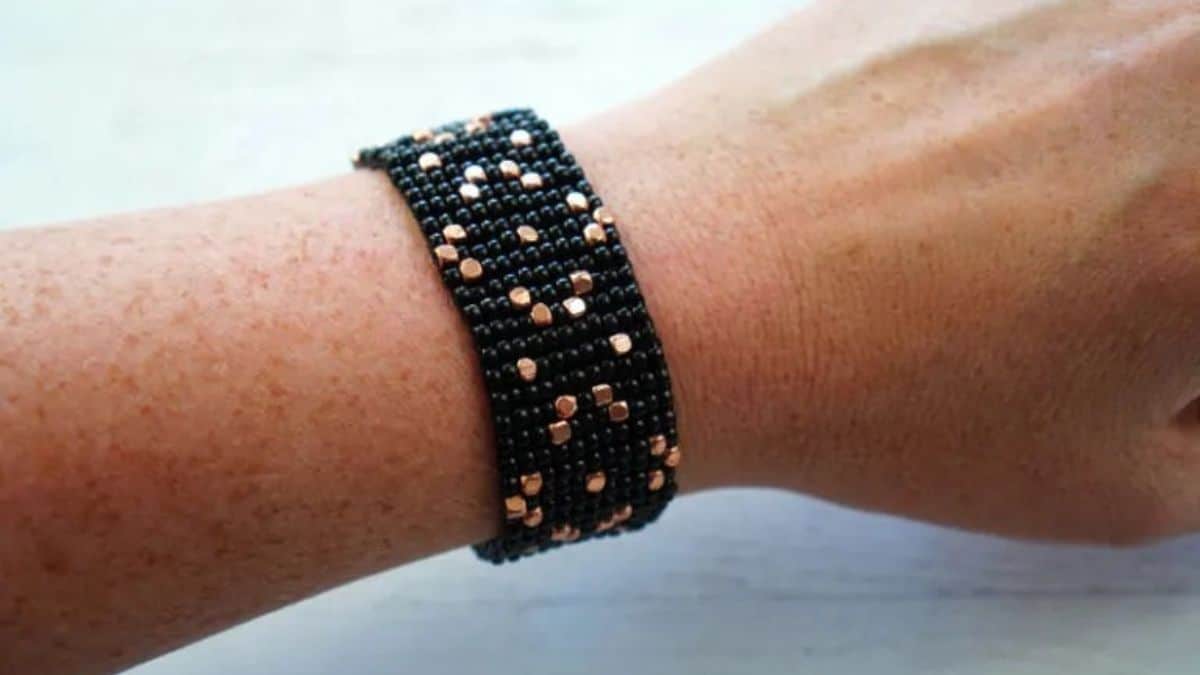 Handmade bead loom bracelet with black seed beads and metallic gold accent beads, creating a bold patterned cuff design worn on the wrist.