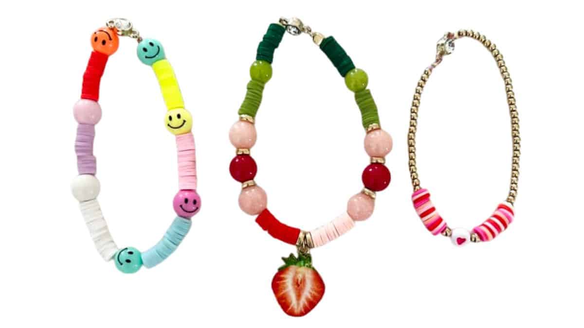 Three colorful clay bead bracelets: one with smiley faces, one with red and green beads plus a strawberry charm, and one with pink striped beads and a heart bead.