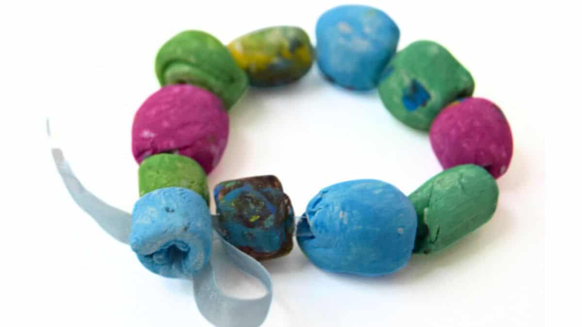 A handmade bracelet with colorful air-dry clay beads in blue, green, pink, and multicolor, tied together with a light blue ribbon.
