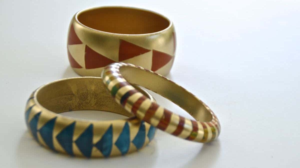 Set of three DIY wooden bangles painted gold with bold geometric patterns in red, blue, and multicolor stripes for a modern, handmade jewelry look.