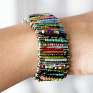 A colorful DIY bracelet made with safety pins strung with multicolored beads, worn on a wrist for a bold handmade jewelry look.