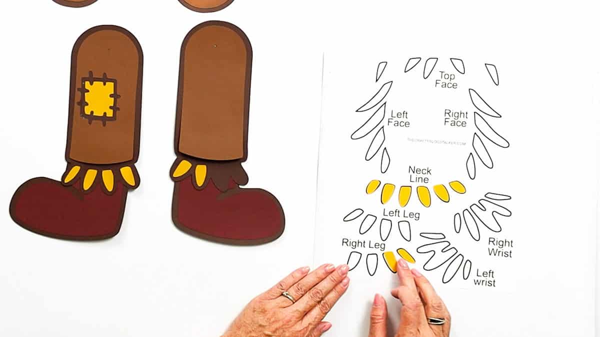 Two completed scarecrow legs with red boots and yellow ankle fringe next to a printable guide for attaching paper fringe pieces in the correct spots.