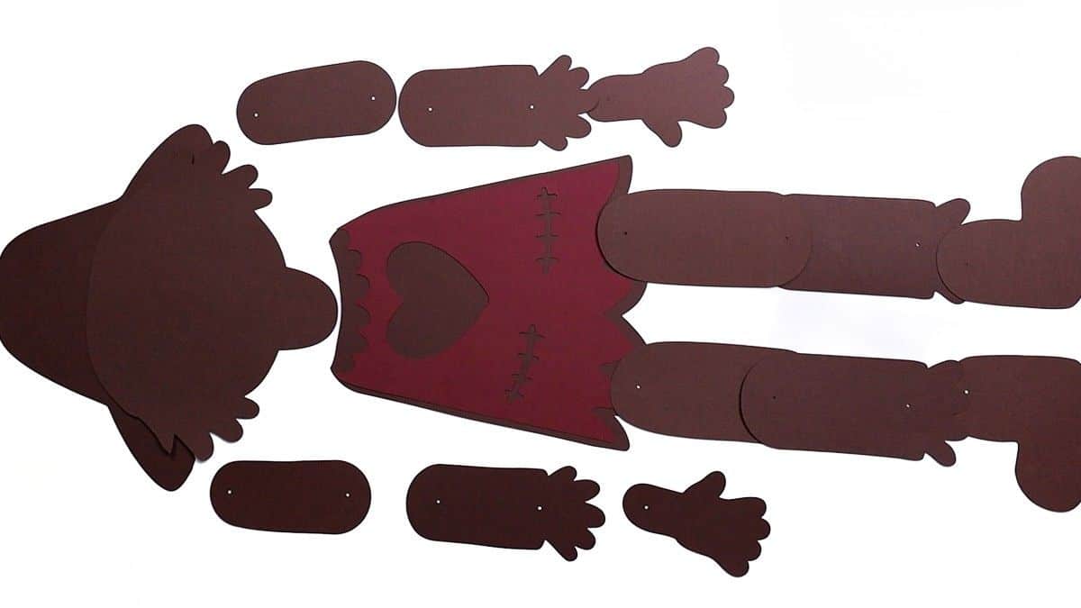 Cut paper base pieces of a scarecrow craft laid out, including hat, body, arms, legs, and shoes, ready to be assembled into a posable figure.