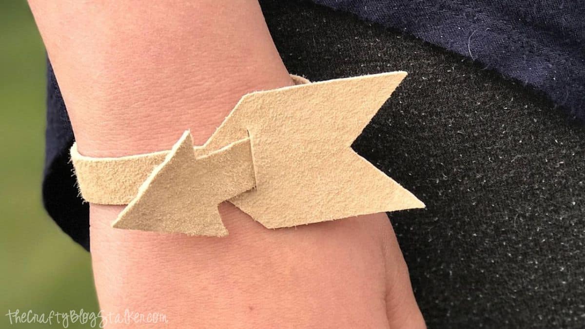 DIY leather arrow bracelet made from light tan suede, worn on a wrist, showing a simple handmade design with overlapping arrow shapes.