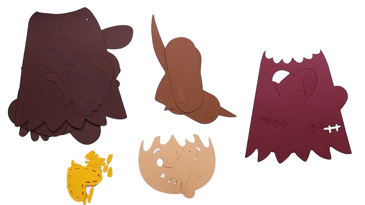 Cut paper pieces for assembling a posable scarecrow craft, including body, arms, legs, face, hair, and clothing parts in fall-themed colors.