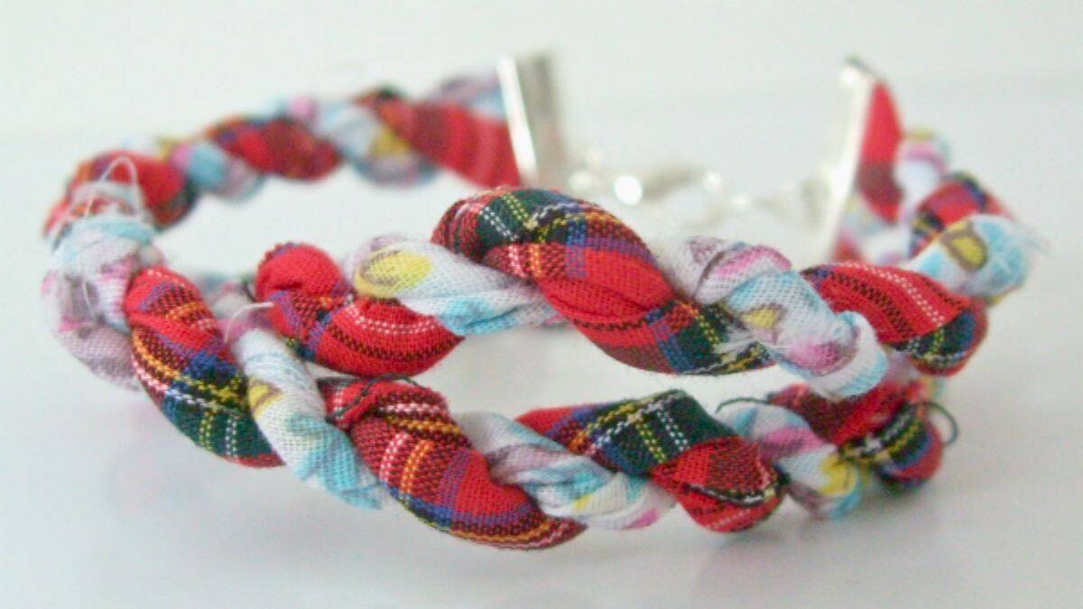 A handmade bracelet crafted from twisted scrap fabric in red plaid and colorful patterns, creating a braided twine design with a metal clasp closure.