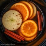 Apple and orange slices with cinnamon sticks simmering in water inside a slow cooker for a cozy fall simmer pot.
