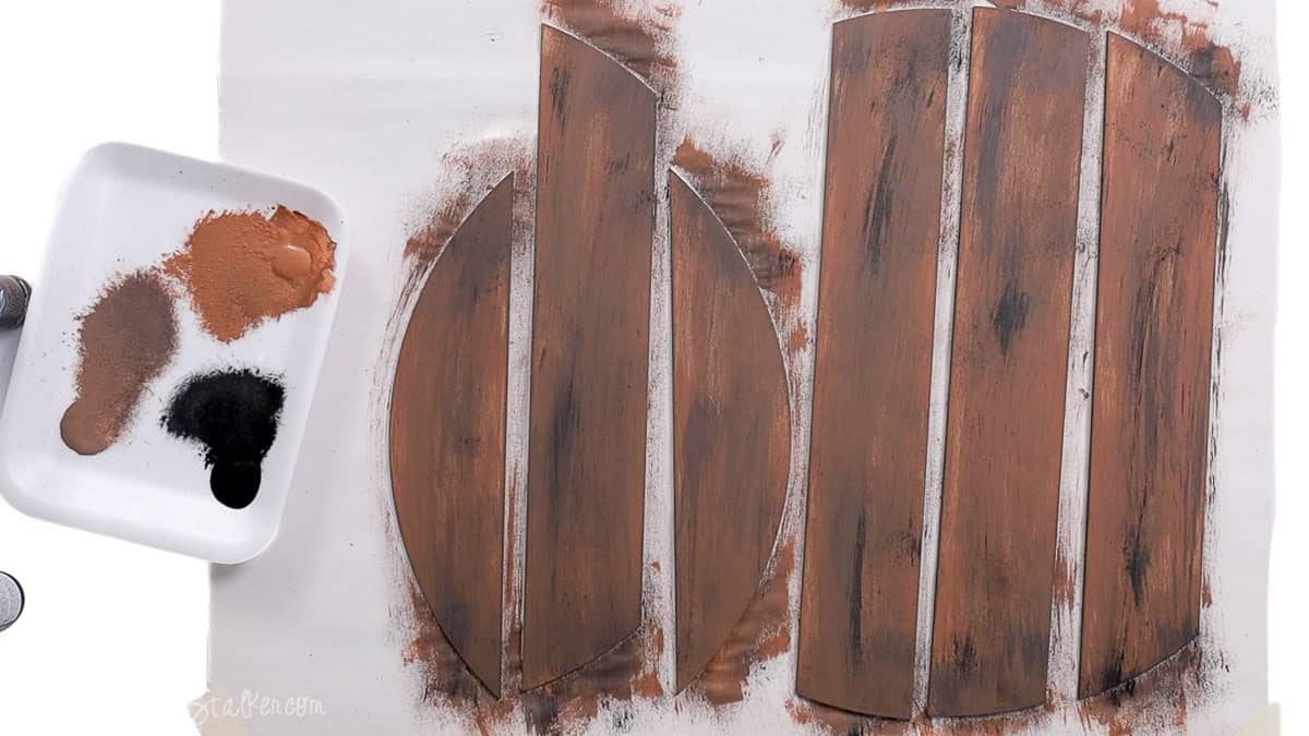 Painted MDF wood door hanger pieces with layered brown and black tones creating a rustic wood grain finish, shown drying on a white surface.