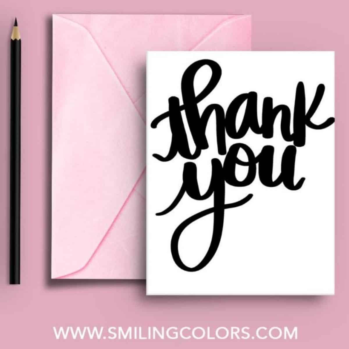White thank you card with bold black hand-lettered text, paired with a pink envelope and black pencil on a pink background.