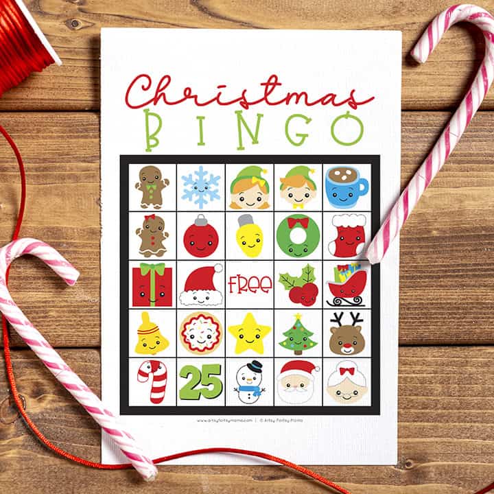 Christmas Bingo game card with cute holiday icons in a 5x5 grid, surrounded by candy canes and ribbon on a wooden table.