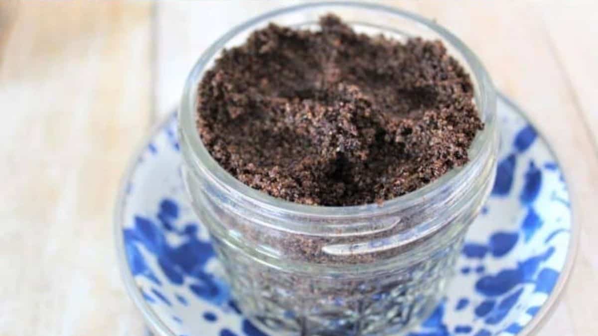 Small glass jar filled with homemade coffee brown sugar scrub sitting on a blue and white patterned plate.