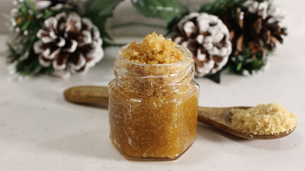 Jar of homemade brown sugar lip scrub with a wooden spoon and pinecone holiday decor in the background.
