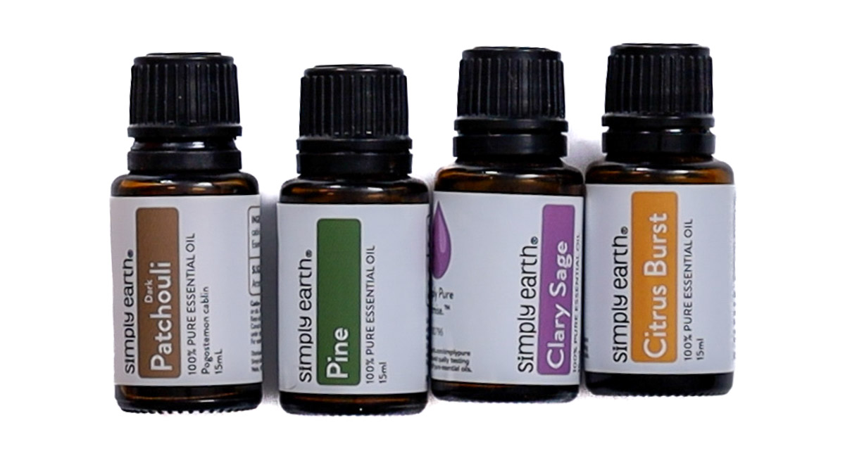 Four bottles of Simply Earth essential oils labeled Patchouli, Pine, Clary Sage, and Citrus Burst, used for scenting DIY candles.