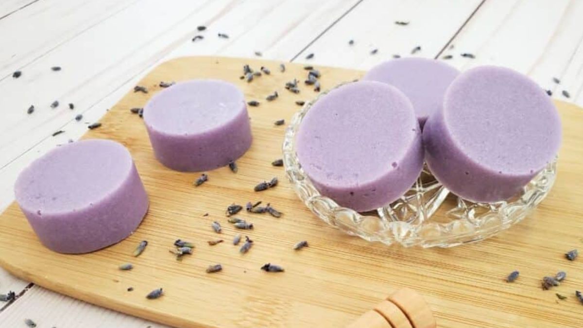 Purple homemade exfoliating sugar scrub bars arranged on a wooden board with dried lavender scattered around.