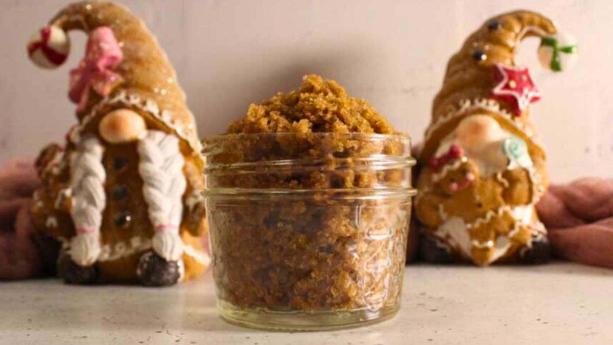 Jar of homemade gingerbread sugar scrub with two festive gingerbread gnome decorations in the background.
