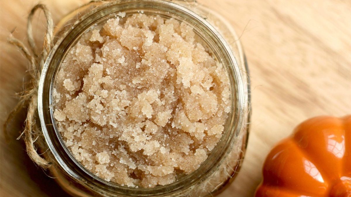 Jar of homemade pumpkin spice sugar scrub wrapped with twine, placed on a wooden surface beside a small decorative pumpkin.