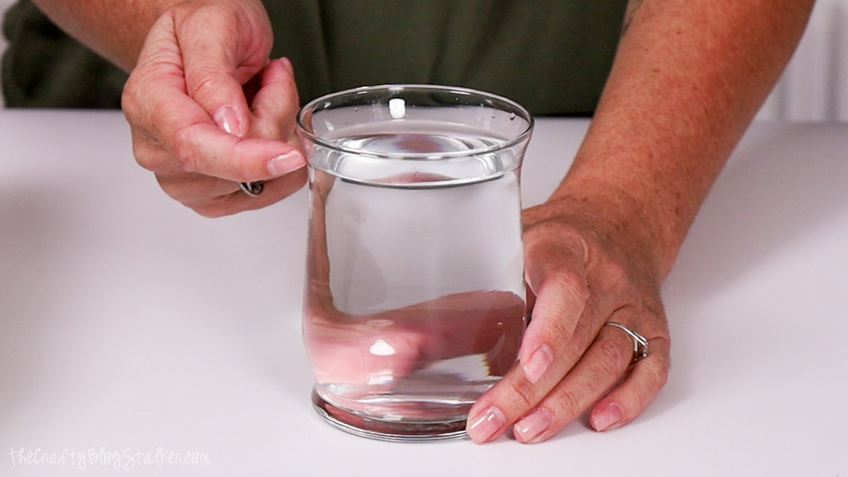 Person measuring the amount of liquid in a glass jar to determine how much wax is needed for a DIY candle-making project.