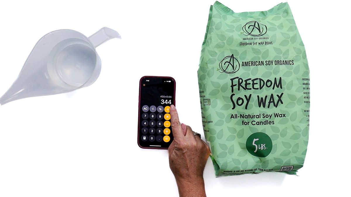 Person using a calculator to measure how much soy wax to melt, shown with a pouring pot and a bag of Freedom Soy Wax for DIY candle making.