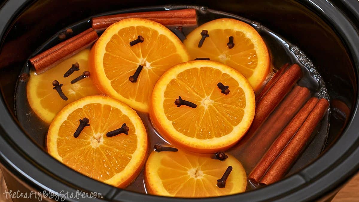 Sliced oranges with cloves and cinnamon sticks simmering in water inside a slow cooker for a homemade holiday potpourri.