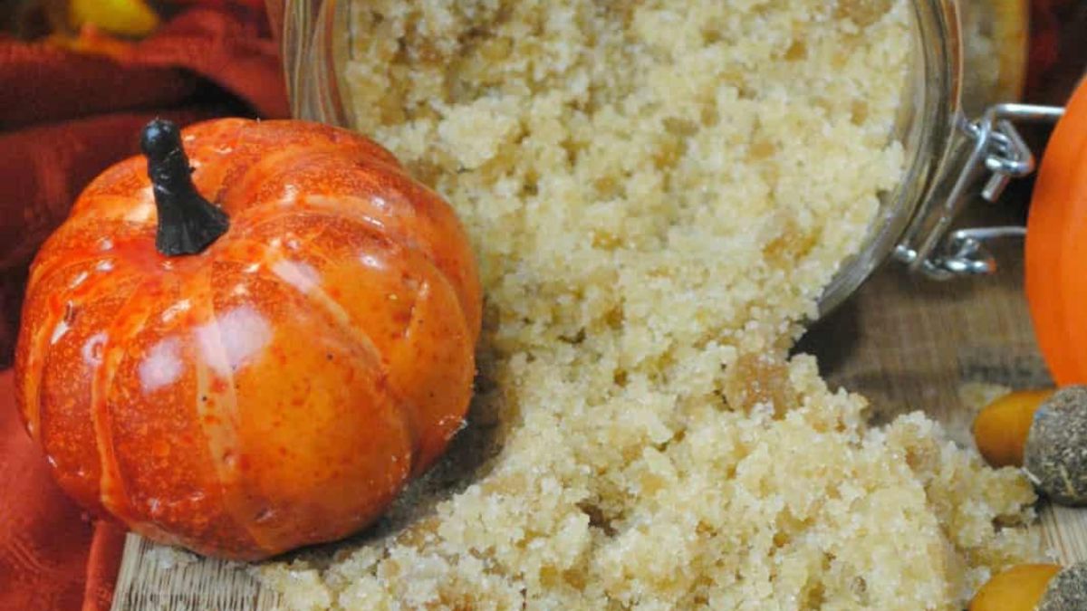 Jar of homemade pumpkin spice sugar scrub spilled onto a wooden surface with a small decorative pumpkin beside it.
