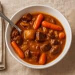 Bowl of slow cooker beef stew with tender beef chunks, carrots, and potatoes in a rich brown gravy, served with a spoon.