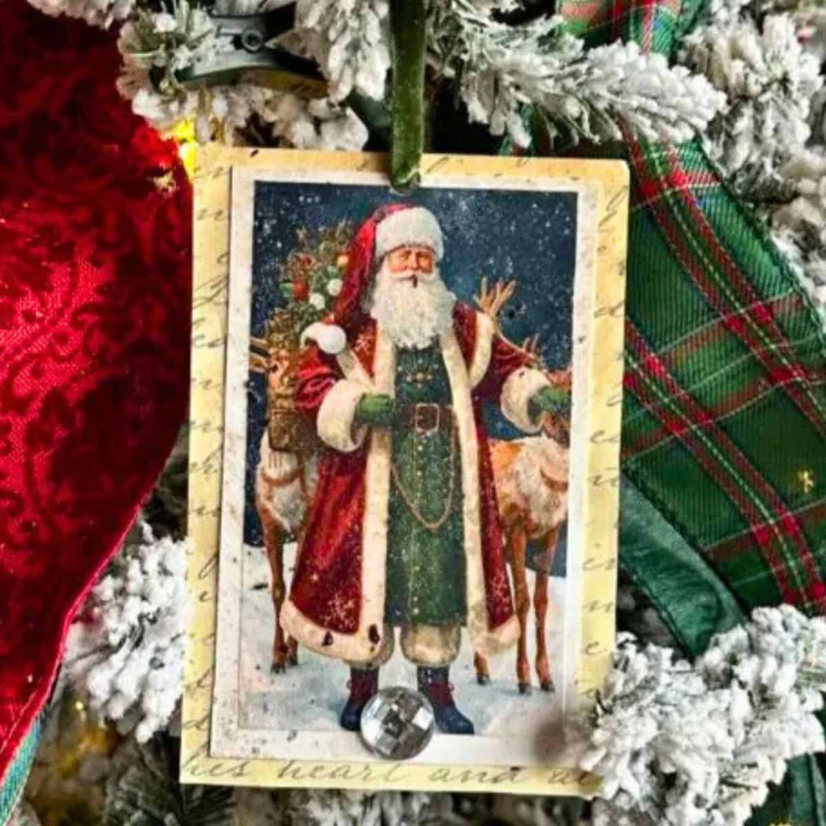Vintage-style Santa tag ornament hanging on a flocked Christmas tree, featuring Santa with reindeer and a ribbon hanger.