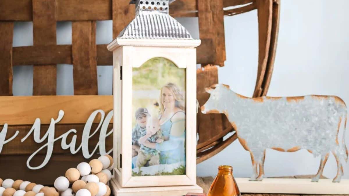 A decorative lantern displaying a family photo, styled on a rustic shelf with wood accents, beads, and a metal cow figurine.