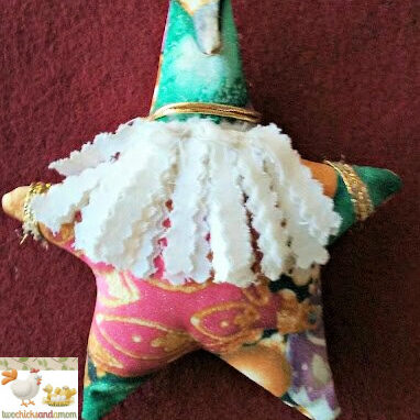 Handmade star-shaped Santa ornament with fabric body, ruffled beard, gold trim, and hanging loop, displayed against a textured background.