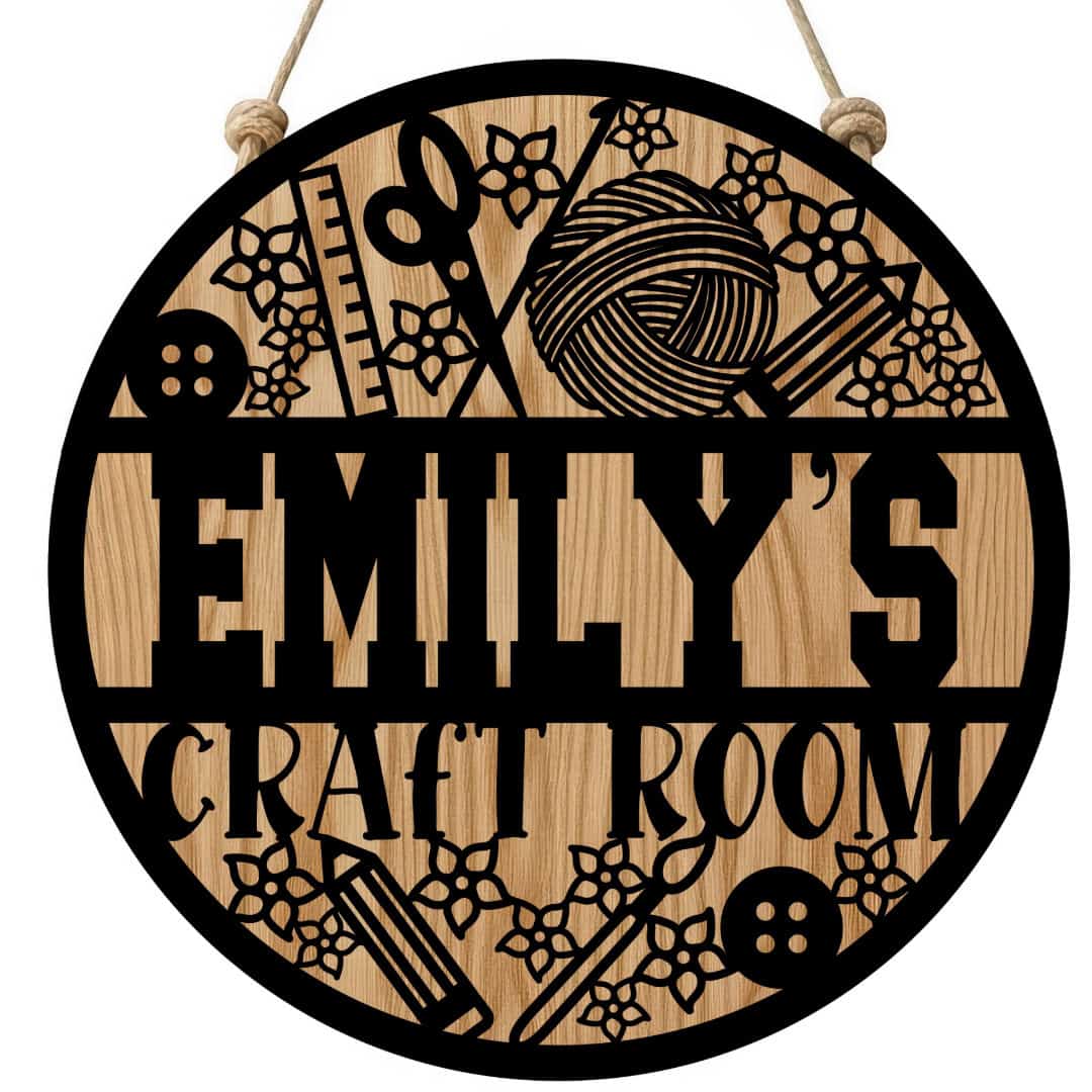 Round wooden door sign reading Emily's Craft Room, decorated with sewing tools, yarn, buttons, and floral accents, hanging by a rope.