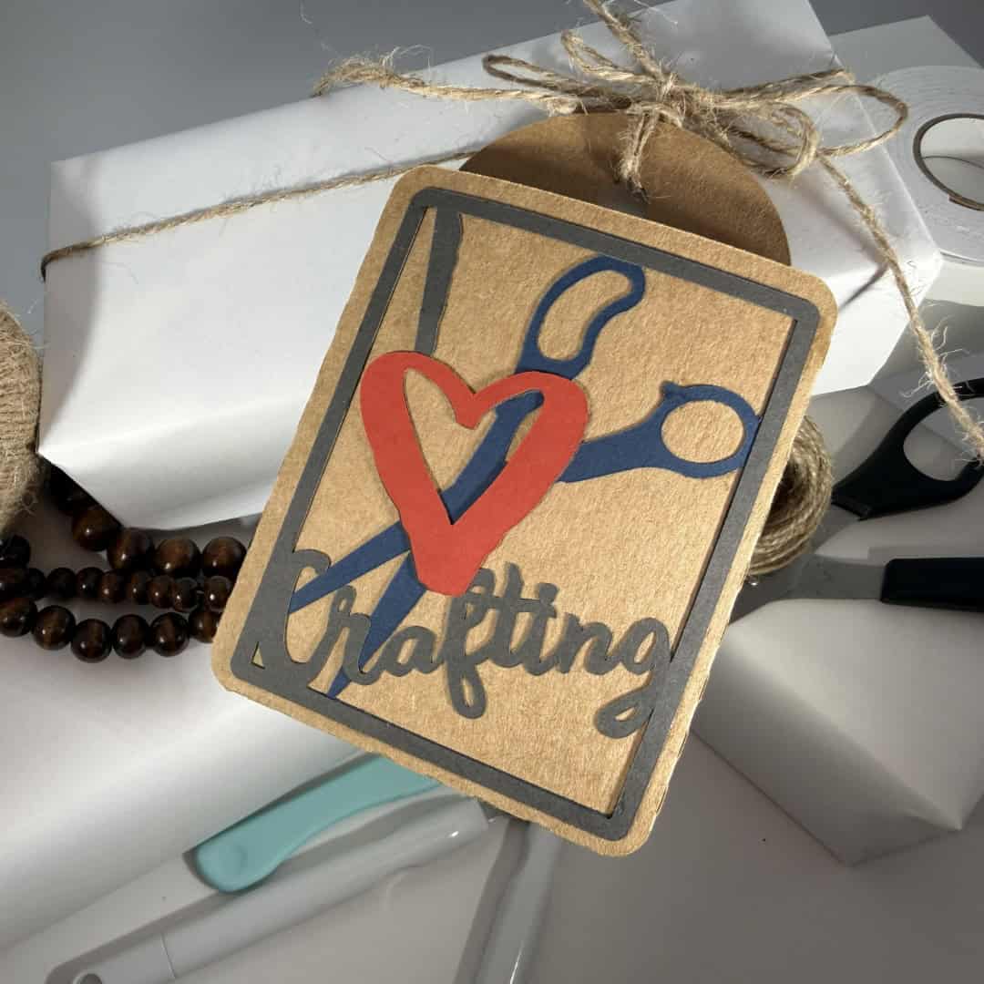 Handmade gift tag with a scissors design and the phrase I love crafting, tied to a wrapped package with twine and craft tools nearby.