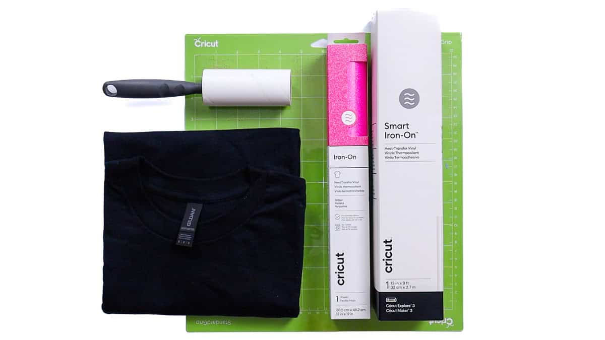 Flat lay of a folded t-shirt, Cricut cutting mat, lint roller, and rolls of iron-on vinyl arranged neatly for a DIY shirt project.