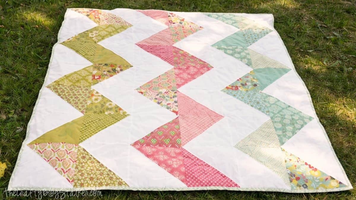 Zig zag patchwork quilt laid flat on grass, showing stitched fabric triangles arranged in a repeating chevron pattern.