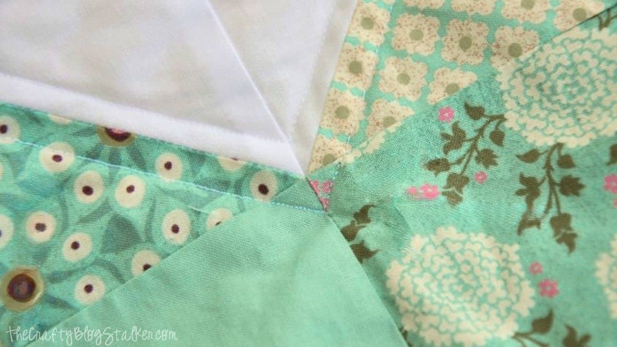 Close-up of quilt seams meeting at a point, showing neatly stitched fabric pieces with floral patterns and precise alignment.