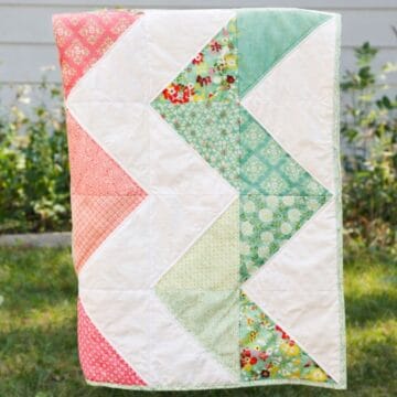 Handmade zig zag patchwork quilt hanging outdoors, showing a chevron pattern made from floral and solid fabric blocks.