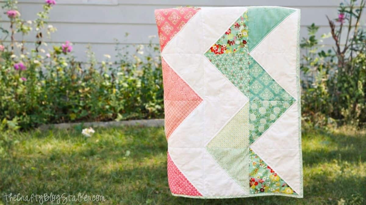 Handmade quilt with a zig zag pattern hanging outdoors on a line, featuring patchwork fabric blocks stitched together.