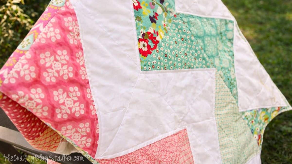 Close-up of a zig zag patchwork quilt draped over a chair outdoors, showing stitched triangles and floral fabric patterns.