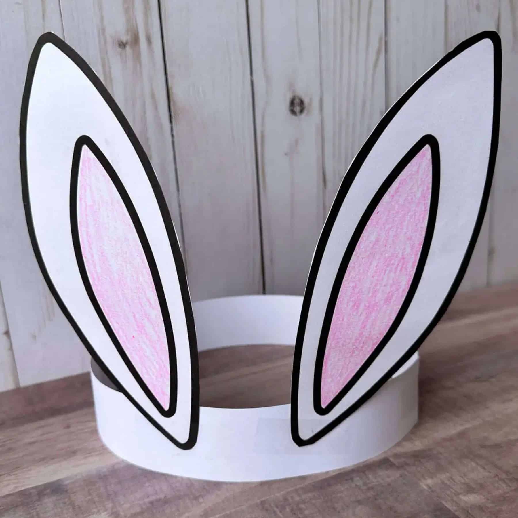 Paper bunny ears headband with two tall ears attached to a white band, displayed on a wooden surface.