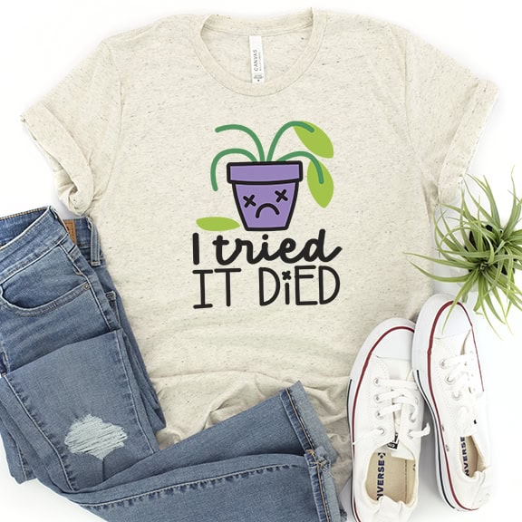 Flat lay of a graphic T-shirt reading I tried it died with a sad potted plant design, styled with jeans, sneakers, and a small houseplant.
