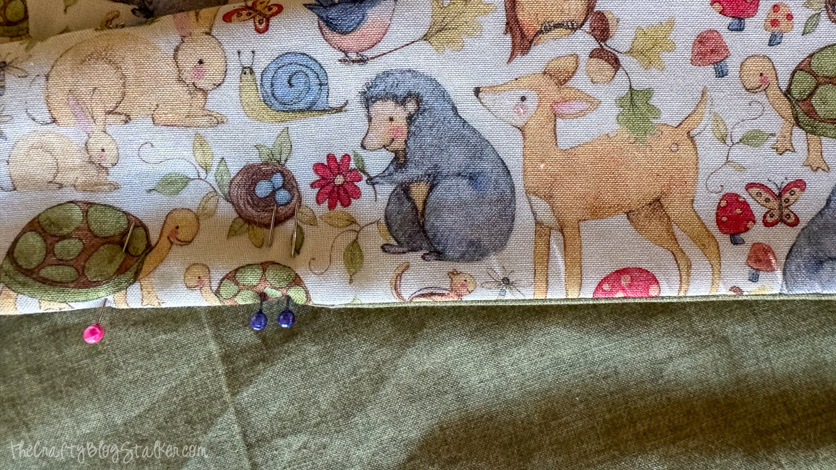 Woodland animal print fabric pinned to green backing, showing a small opening left unsewn for turning the baby blanket.