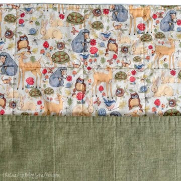 Handmade baby blanket with woodland animal print on one side and solid green fabric on the other, showing straight quilting lines.