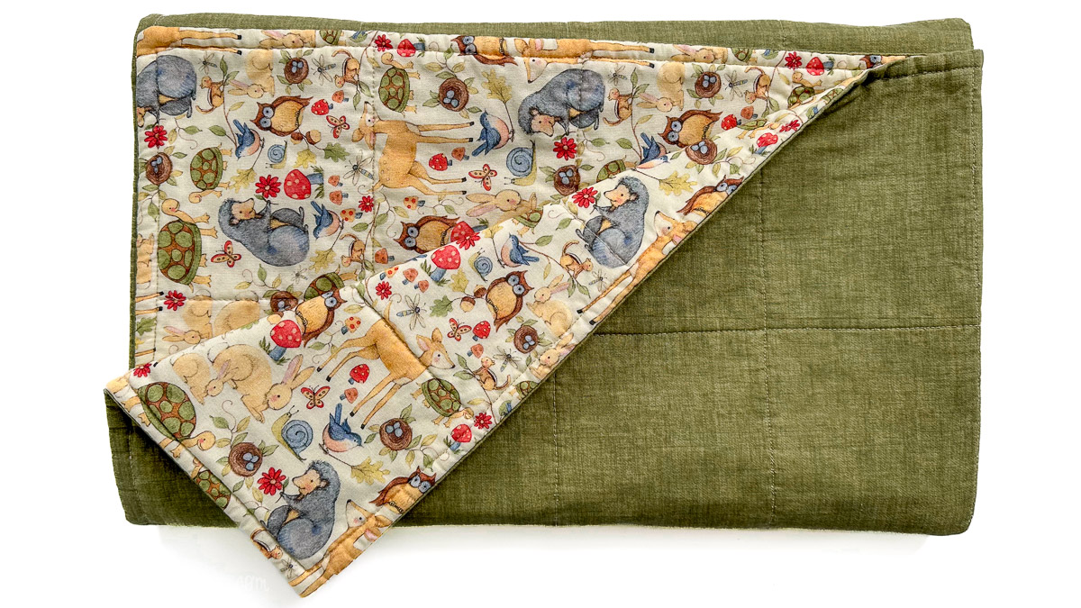 Finished baby blanket folded to show green backing and woodland animal print front with visible quilting lines.