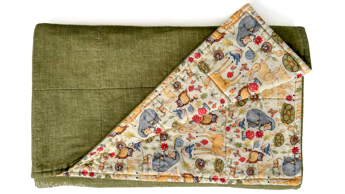 Handmade baby blanket with solid green fabric backing and woodland animal print front featuring deer, owls, turtles, and flowers.