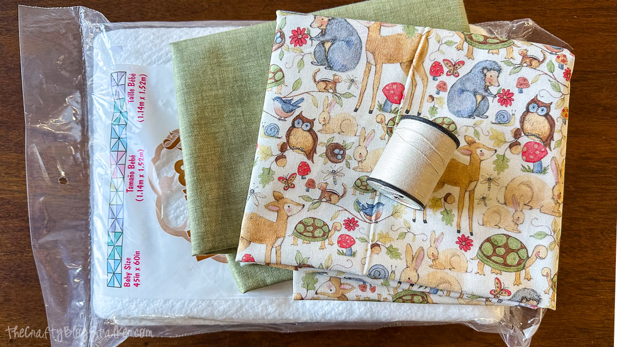 Baby blanket supplies including woodland animal fabric, green backing fabric, white thread spool, and a packaged batting insert.