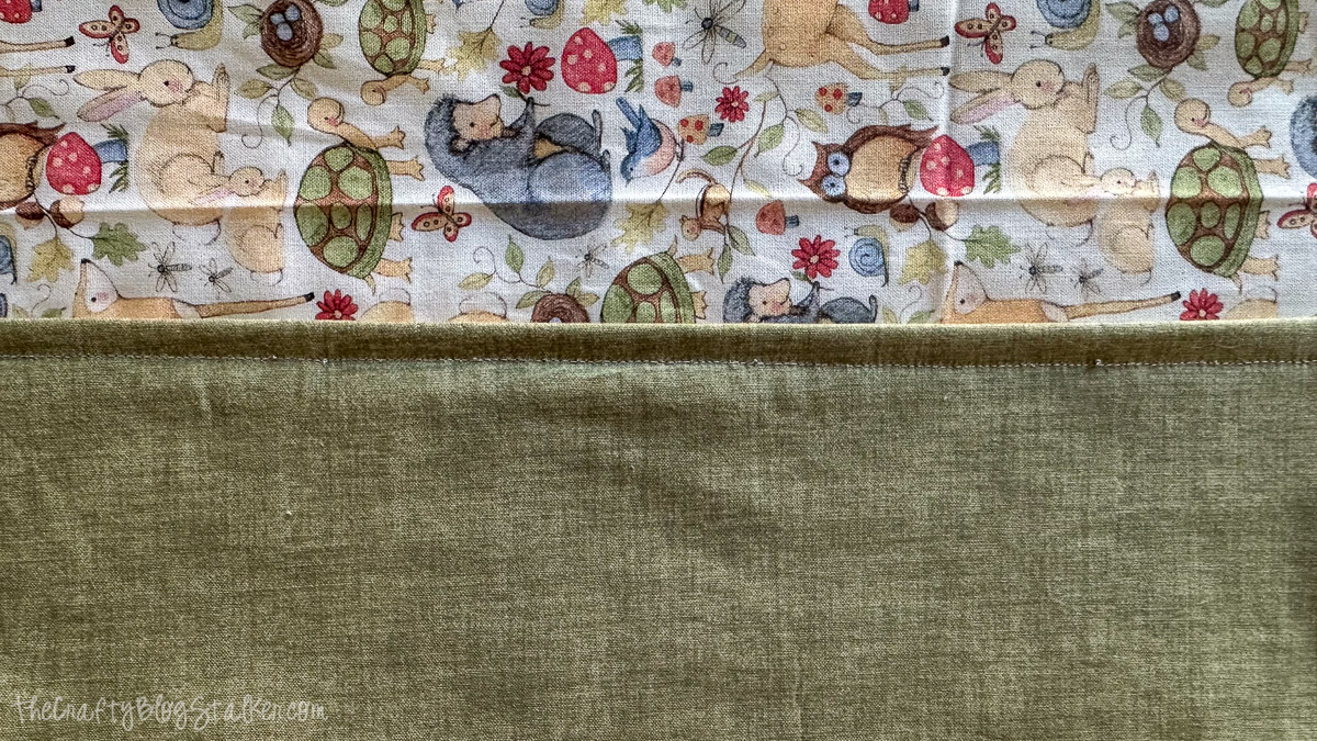 Close up of baby blanket edge with woodland animal print and green backing, showing topstitching along the seam.