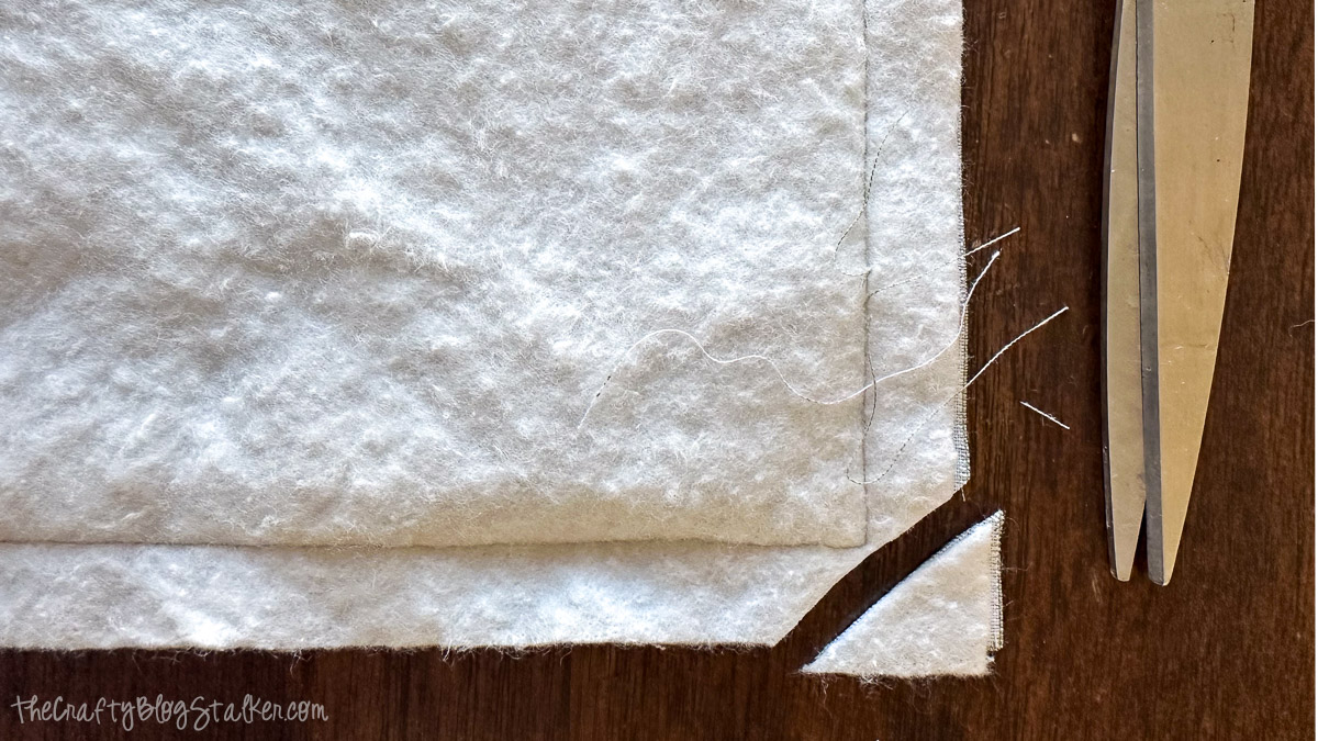 Corner of baby blanket trimmed at an angle with scissors, showing batting layers and clipped seam allowance.