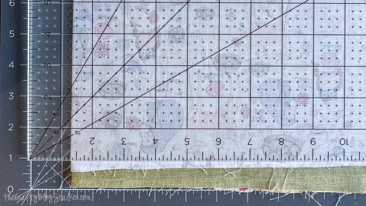 Quilting ruler and rotary mat aligned along layered fabric to trim uneven edges straight before sewing.